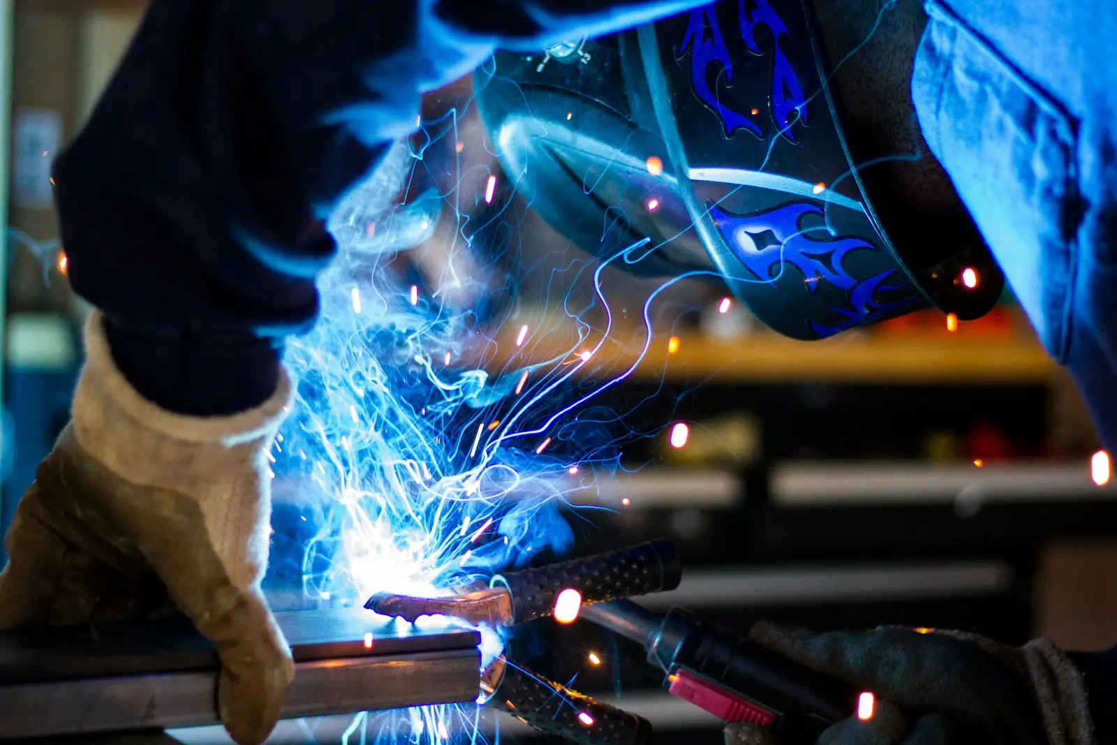 A welder in a protective helmet working on metal as sparks fly